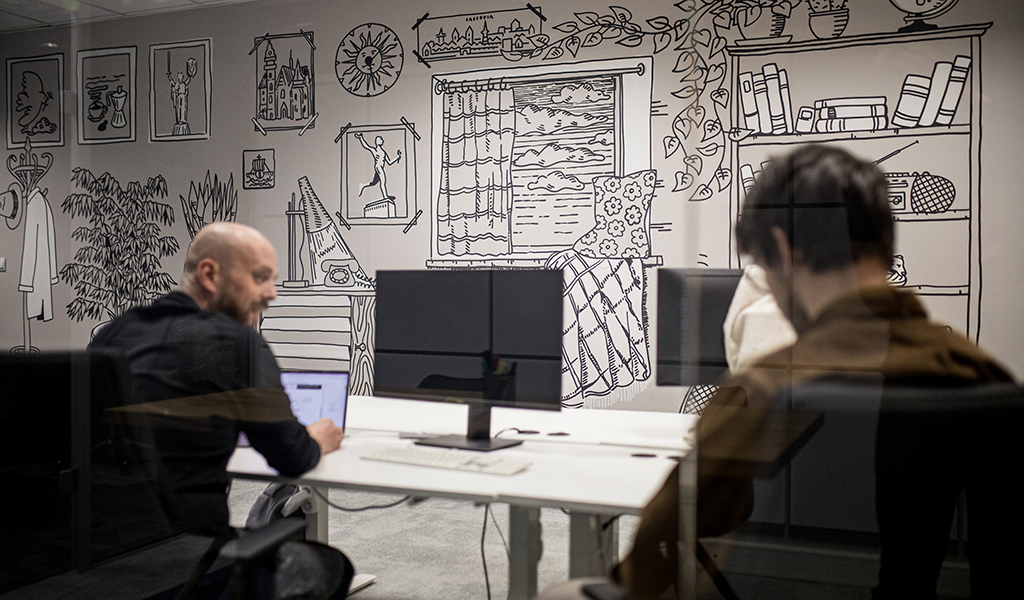 Office wall with custom illustrations and two team members discussing work