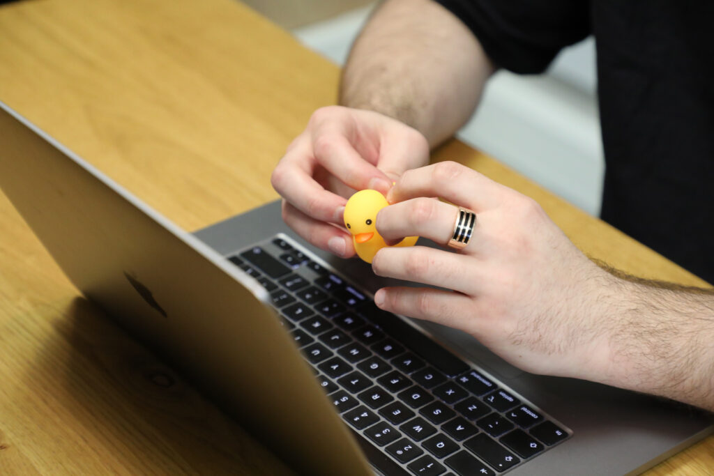 detail of a male hands holding a rubber duck near a laptop