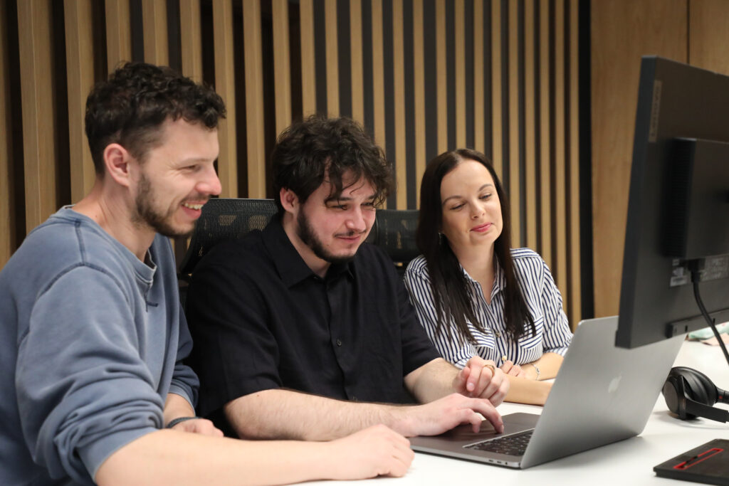 three colleagues smiling and looking into one laptop